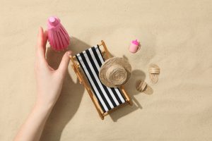 female hand and mini beach accessories on sand background