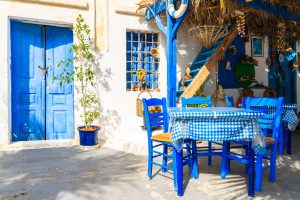 table in front of typical greek house on street of finiki village, karpathos island, greece