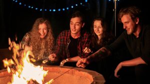 a group of happy young friends near a campfire at glamping, night