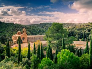 view of the fontfroide abbey (wine clad monastery) surrounded by trees and mountains with a sky full of clouds, narbonne, france.
